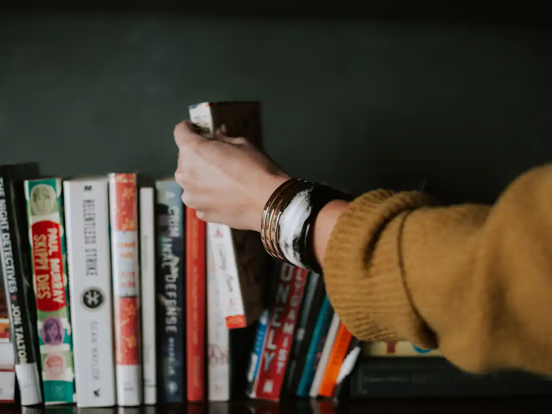 Eine Hand zieht ein Buch aus einem gefüllten Regal